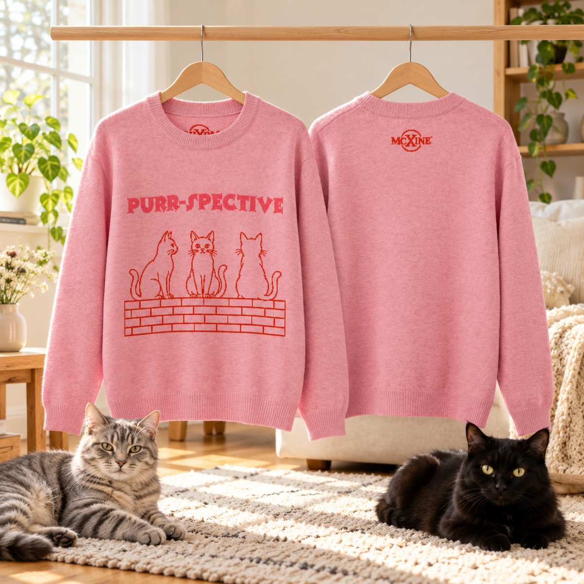 Two pink Purr-spective cat jumpers on hangers with two cats on a rug below